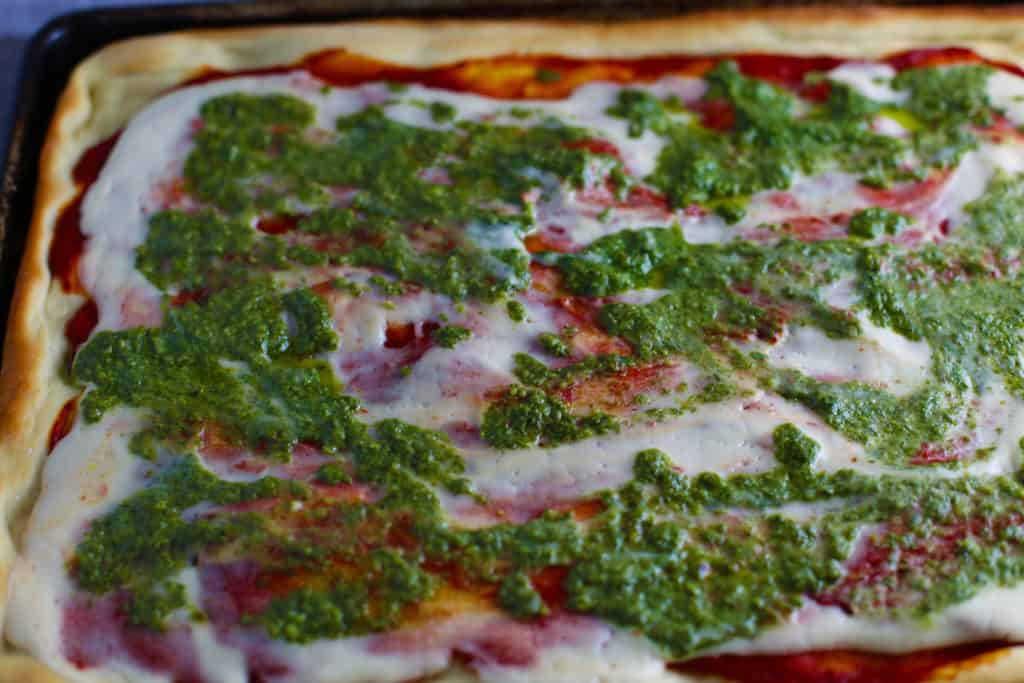 vegan mozzarella on top of pizza with tomato sauce and basil pesto