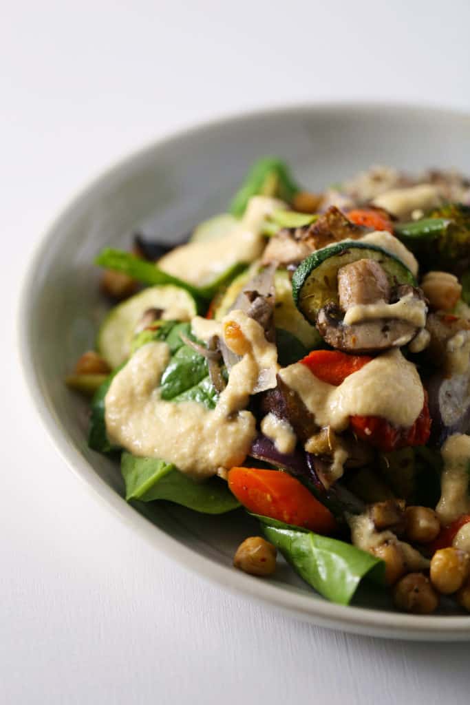 A bowl of roasted vegetables and chickpeas drizzled with lemon tahini sauce