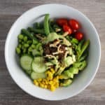 Bowl with sliced cucmber, tomatoes, asparagus, green beans, edamame, mushrooms, and corn. Drizzled with avocado green goddess dressing.