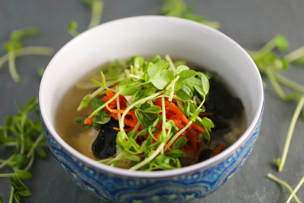 vegan miso soup in a bowl with sushi rice, pea shoots, and grated carrots