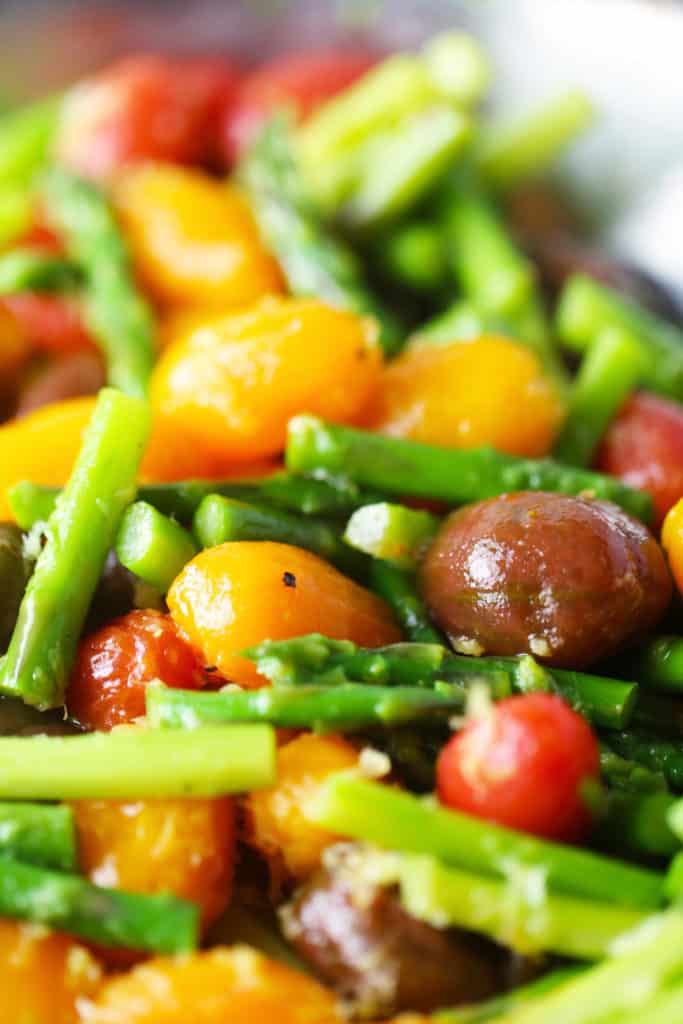 A dish of cooked asparagus and various colored cherry tomatoes.