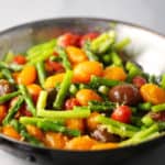A dish of cooked asparagus and various colored cherry tomatoes.