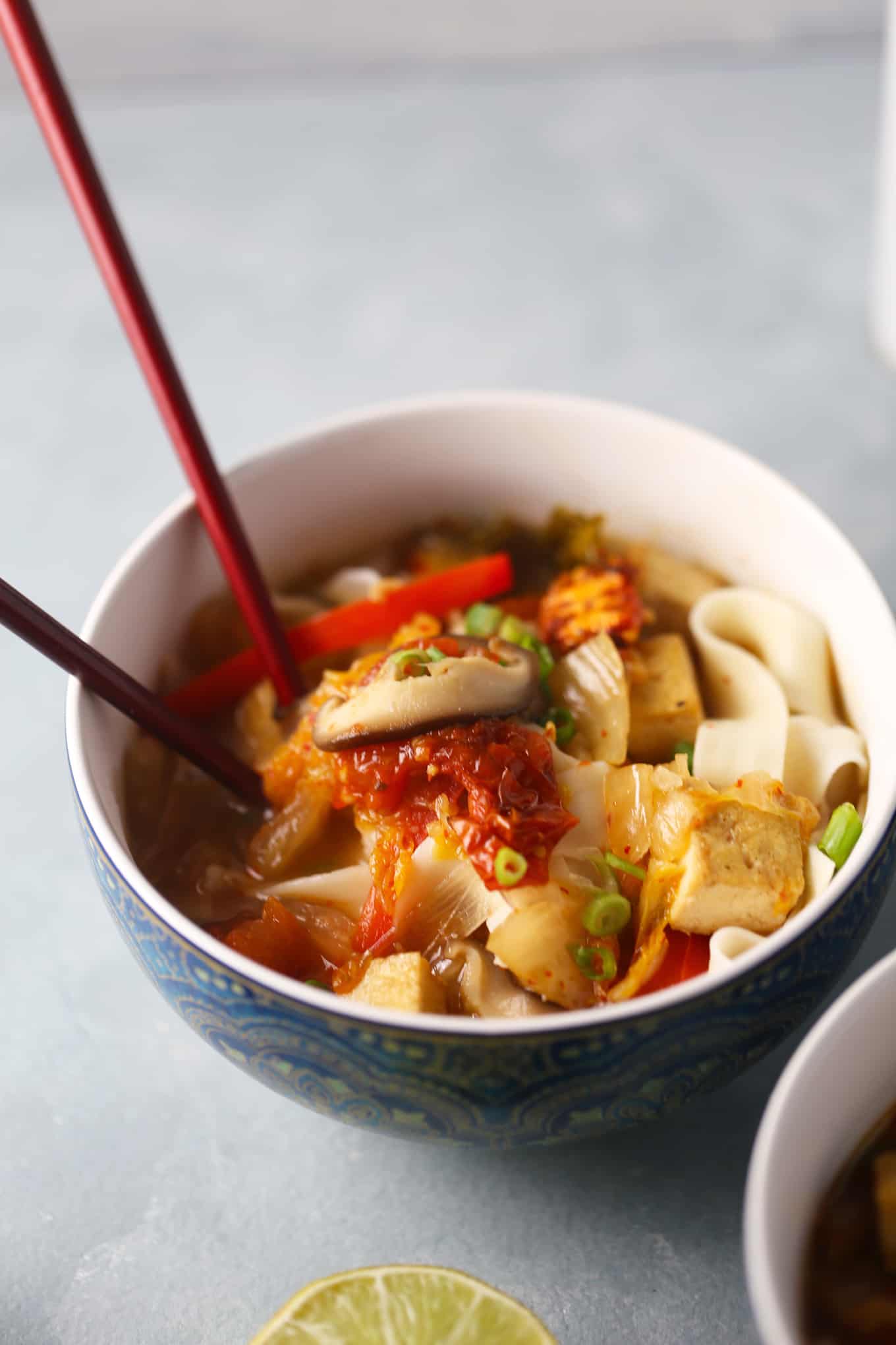 A bowl of Japanese Udon Noodles with tofu and a kimchi miso broth, with chopsticks.