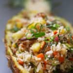 A pineapple half filled with fried rice and vegetables.