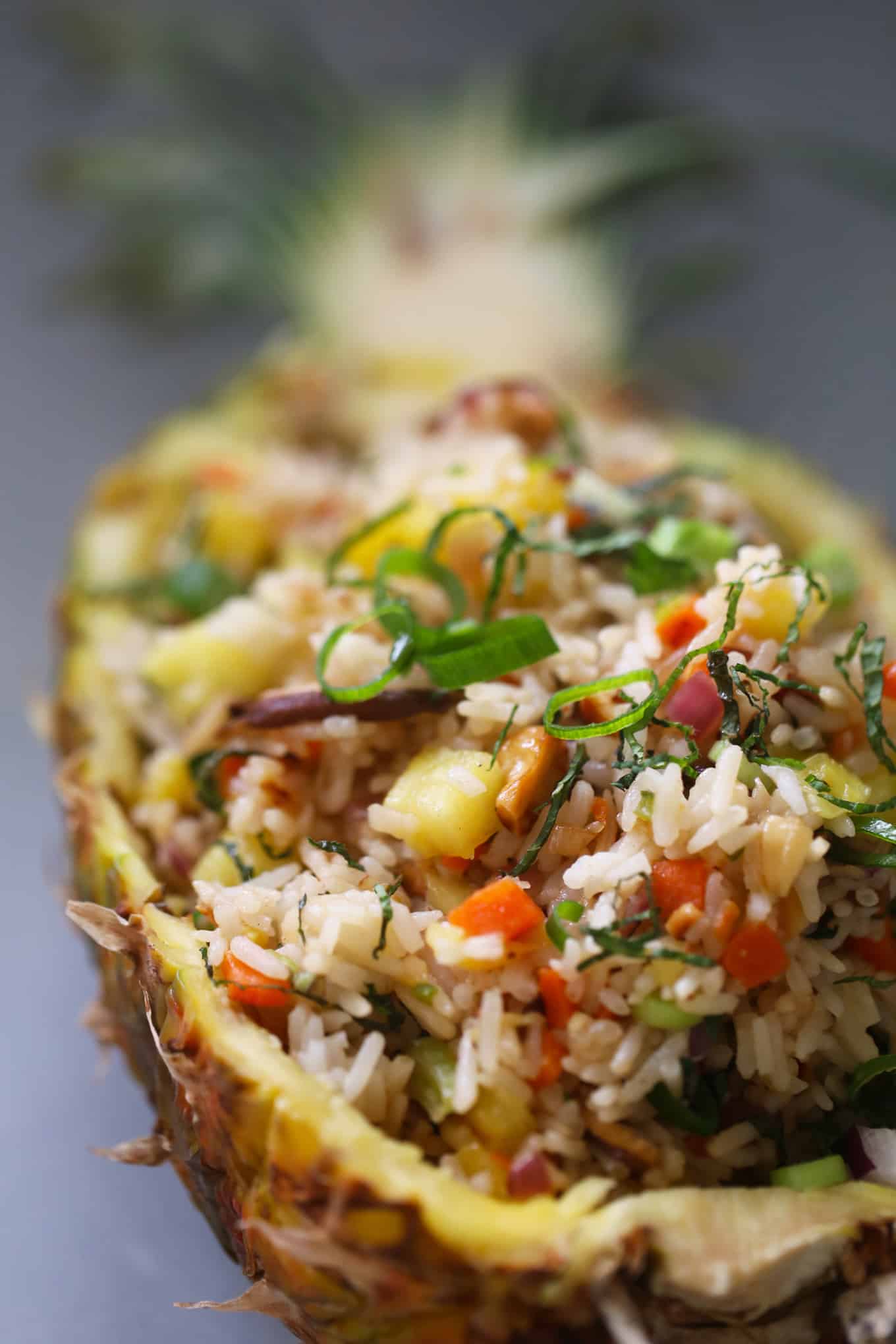 A pineapple half filled with fried rice and vegetables.